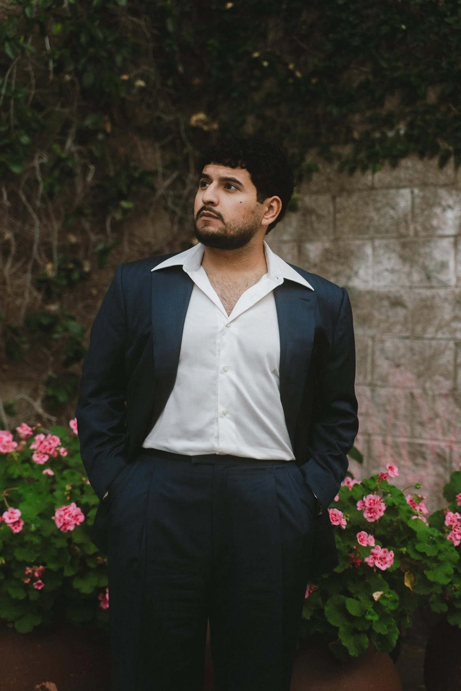 Man in a bespoke navy Ermenegildo Zegna wool suit by By Fino Los Gatos, standing against a garden wall