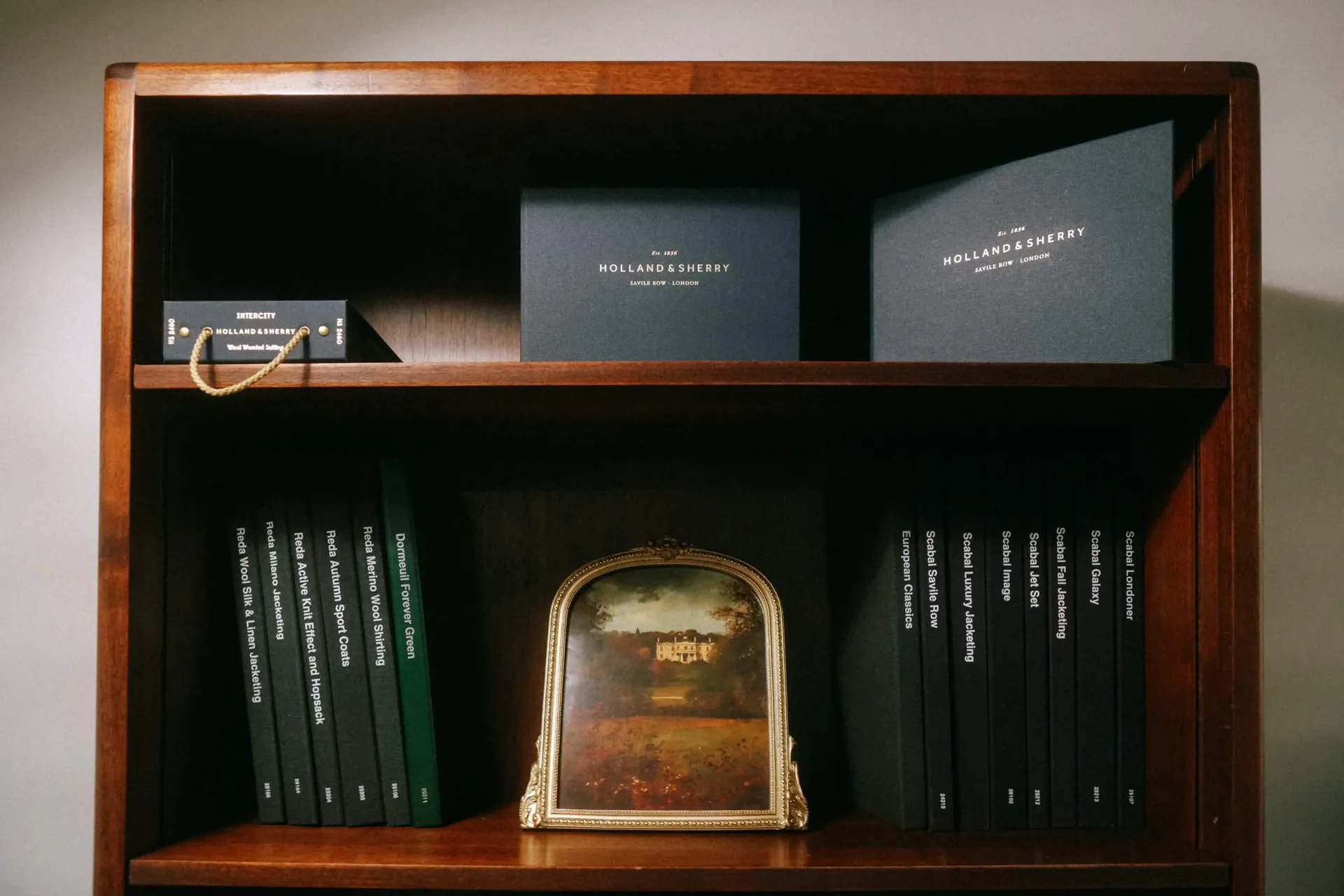 Fabric swatch books arranged on mahogany shelves alongside Holland & Sherry boxes
