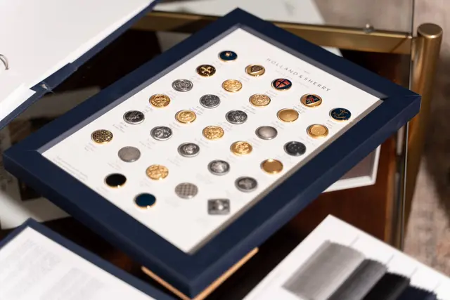 A tray of suit buttons beside cloth swatches