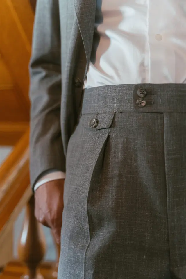 Close view of a trouser waistband with side adjusters and a forward pleat