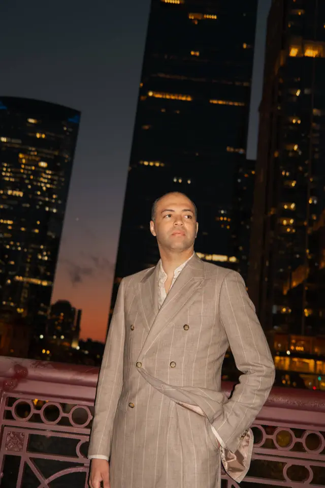David in a double-breasted suit against city lights at dusk